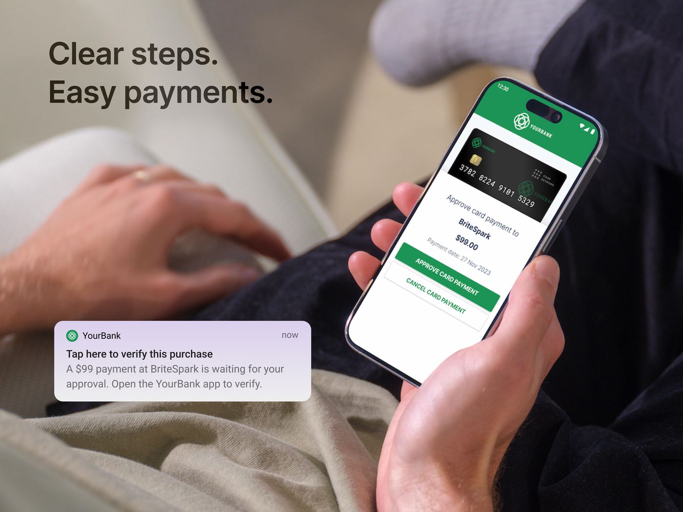 A person on a sofa approving a card payment in a banking app on their phone, with a clear two-step checkout screen.